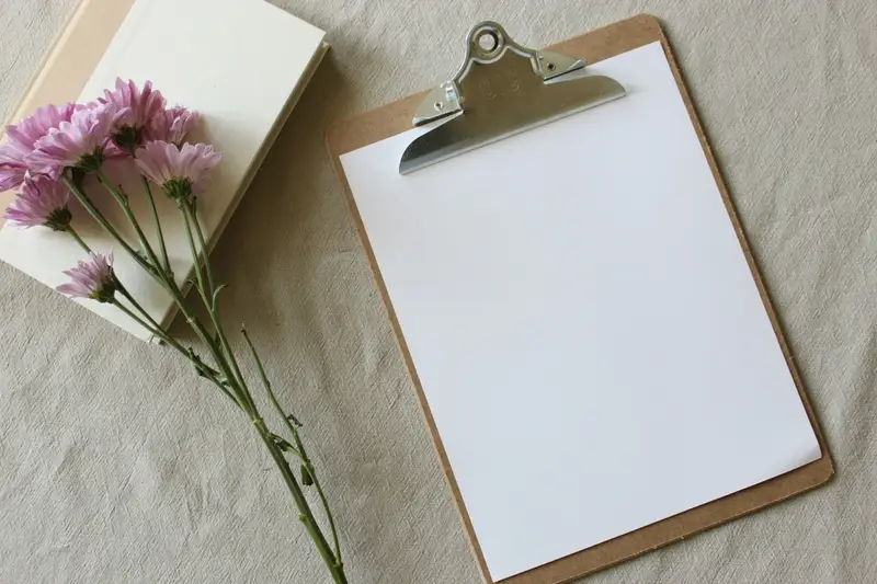 Prancheta com uma folha em branco e flores ao lado.